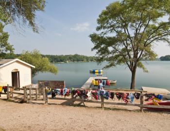View of beach at Summer Camp with boat house, changing room, wooden fence with life jackets and life