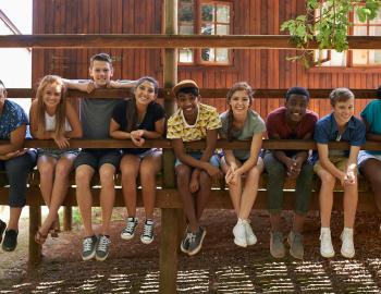 kids sitting on the deck of a camp cabin with legs dangling over the edge, arms propped on rails
