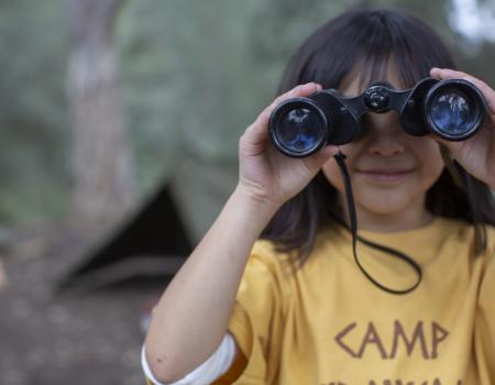 Portrait cute girl bird watching at summer camp with binoculars