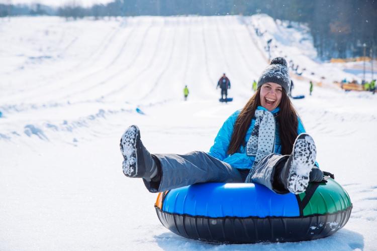 a woman smiles at the foot of a snow tubing hill