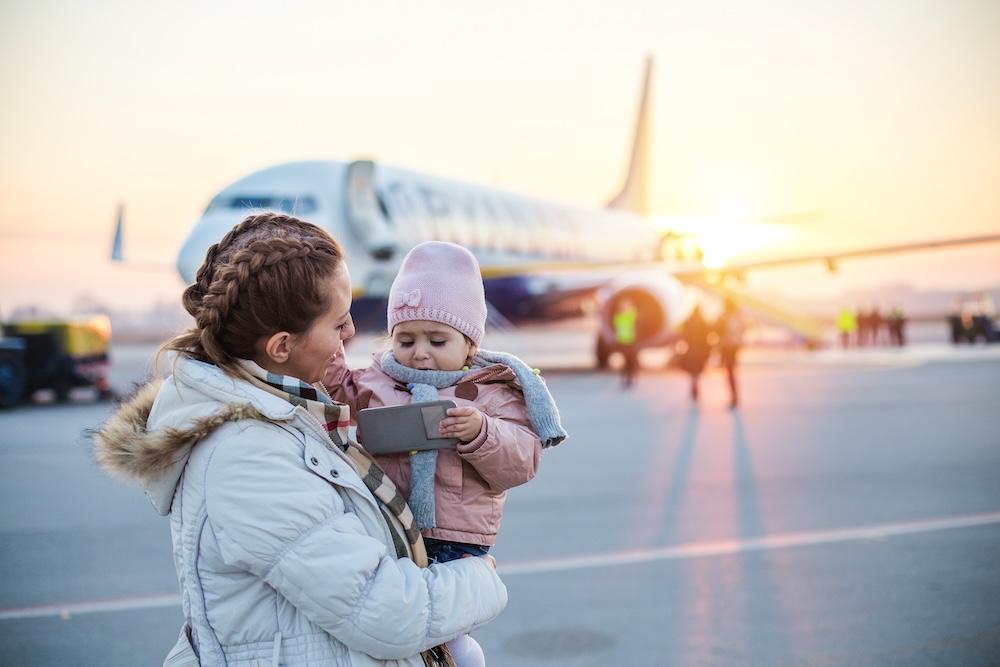 mother and baby standing on tarmac with plane in background in winter 