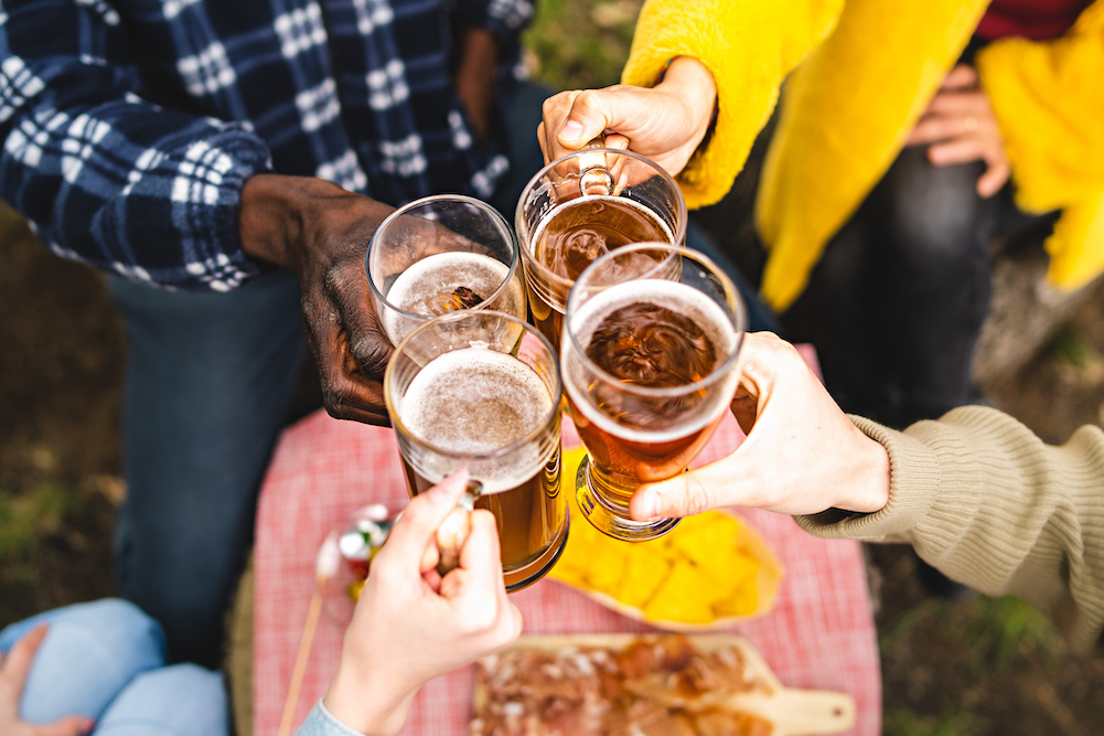 4 people outside raising glasses of beer to cheers