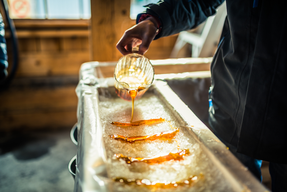 A close-up of a person at sugar shack pouring maple syrup onto snow to make maple sugar taffy