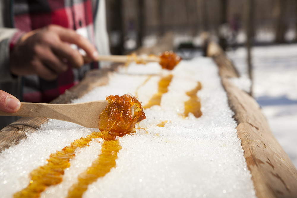 warm maple syrup on snow getting rolled up with wooden spoons