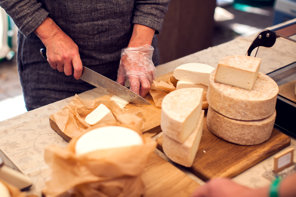 person slicing cheese with several wheels of various cheese displayed around them