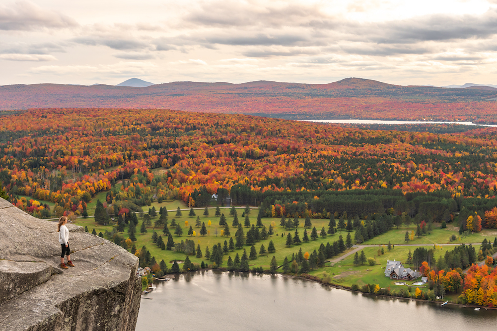 woman standing at top of mountain overlooking fall leaves of Vermont forests